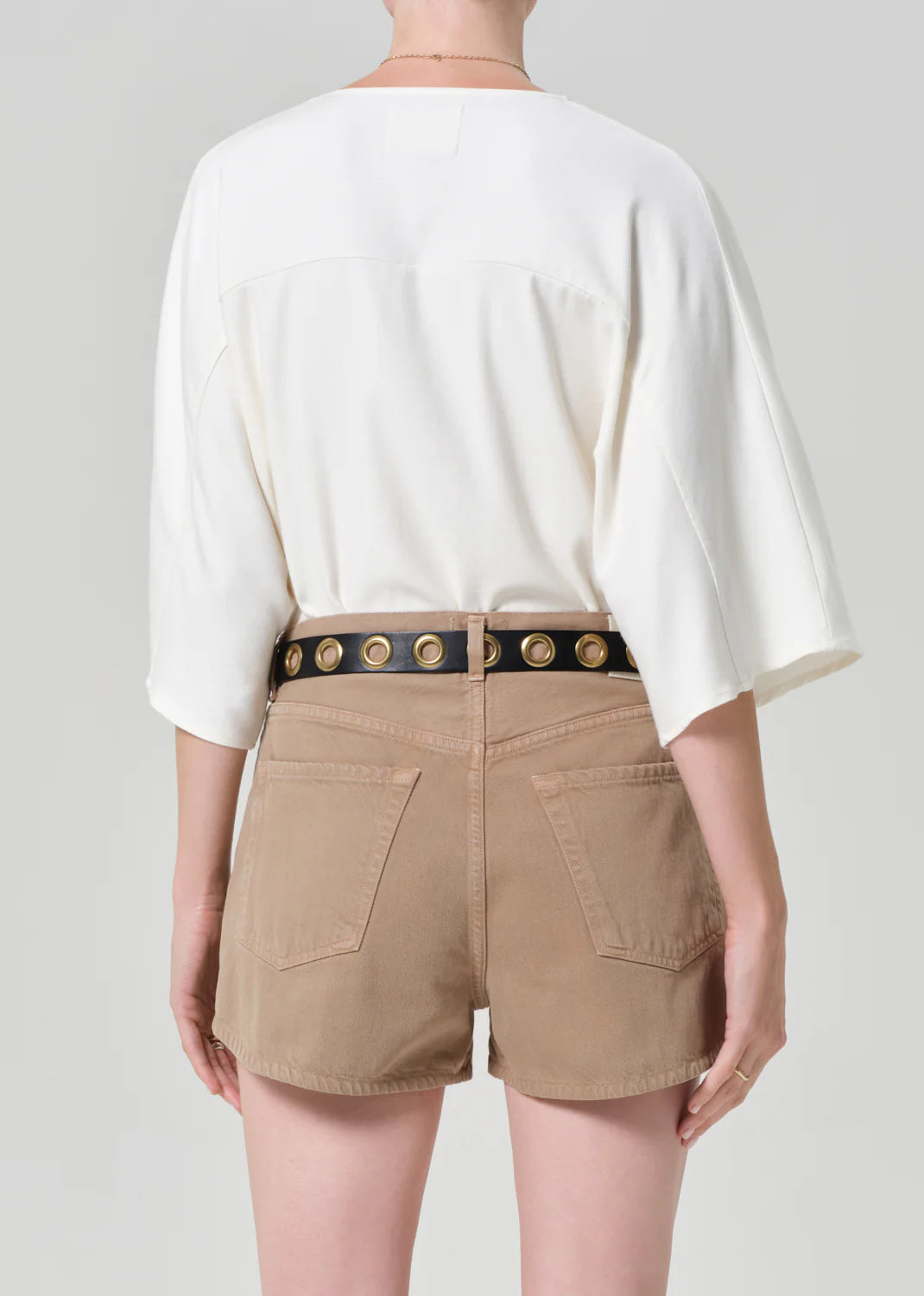 Back view of woman wearing Citizens of Humanity oversized white button-up shirt with tan shorts and studded belt.