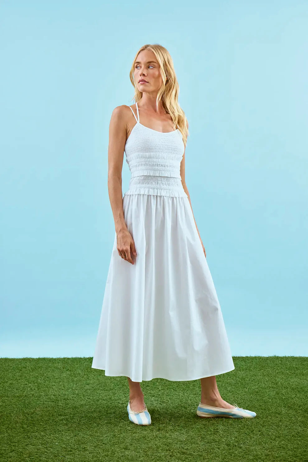 Woman wearing Hunter Bell Francie white sleeveless midi dress with smocked bodice and flowing skirt, standing on grass.