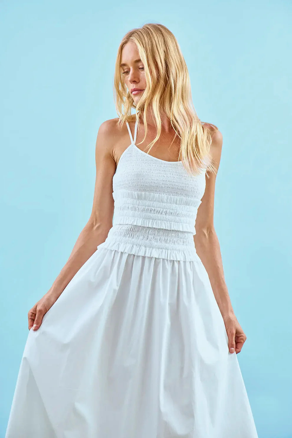 Hunter Bell Francie white halter dress with smocked bodice and flowing skirt on model against blue background.