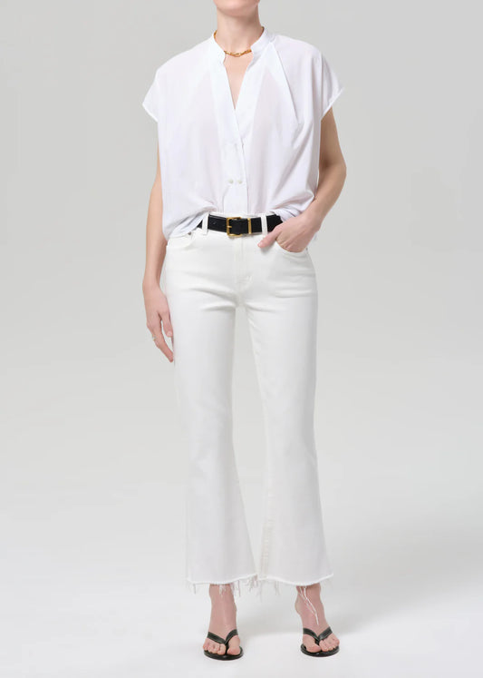 Woman wearing Citizens of Humanity white kick flare jeans with raw hem, white button-up shirt, and black sandals.