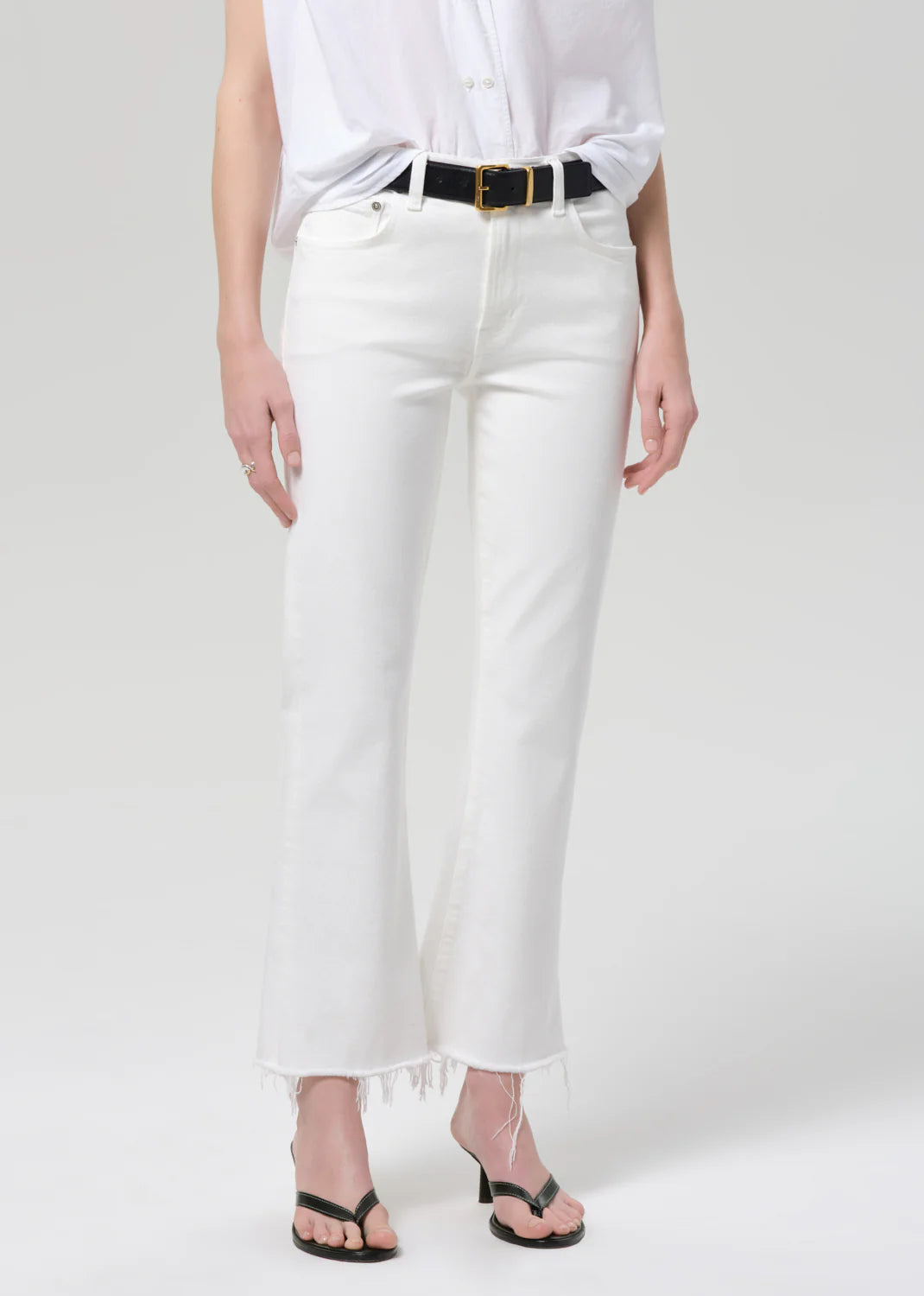 Citizens of Humanity white high-waisted kick flare jeans with raw frayed hem, styled with black belt and heeled sandals.