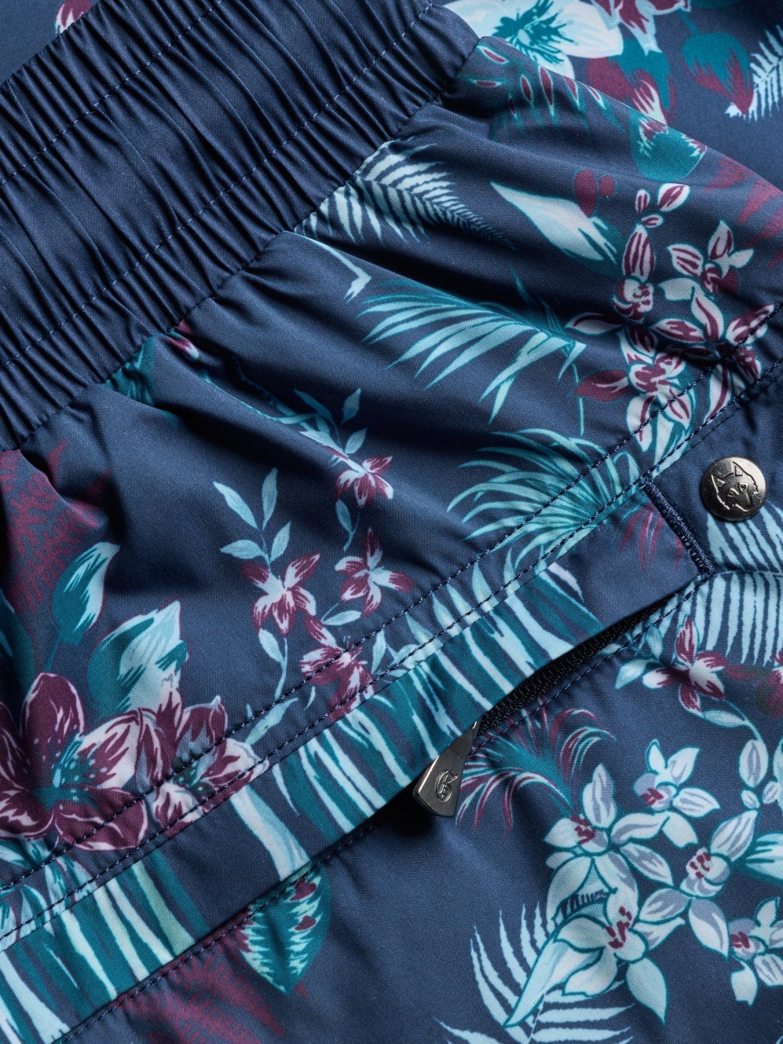 Close-up detail of navy swim shorts with tropical floral pattern showing elastic waistband and pocket