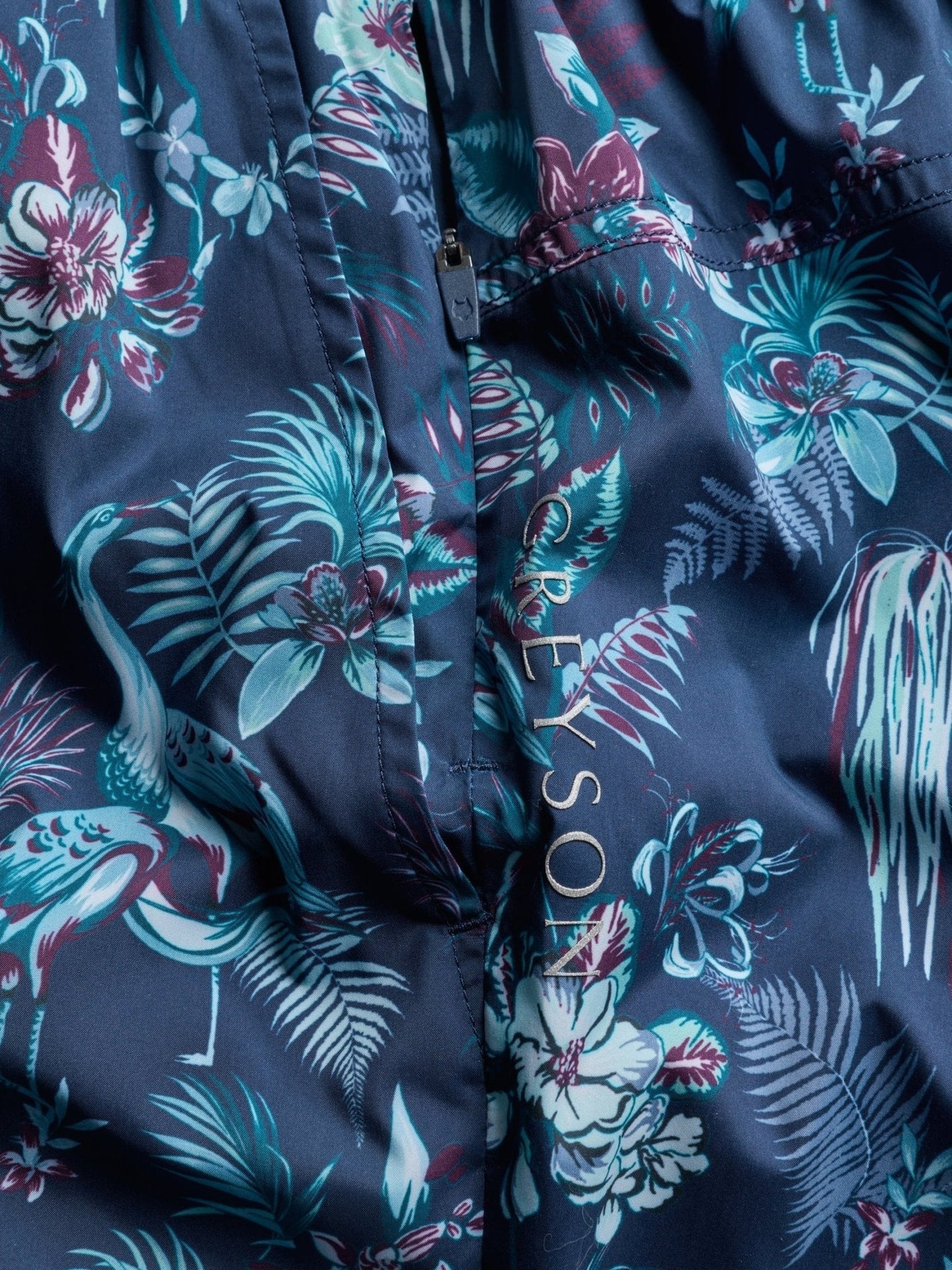 Close-up detail of navy blue swim shorts with tropical floral pattern and Greyson branding