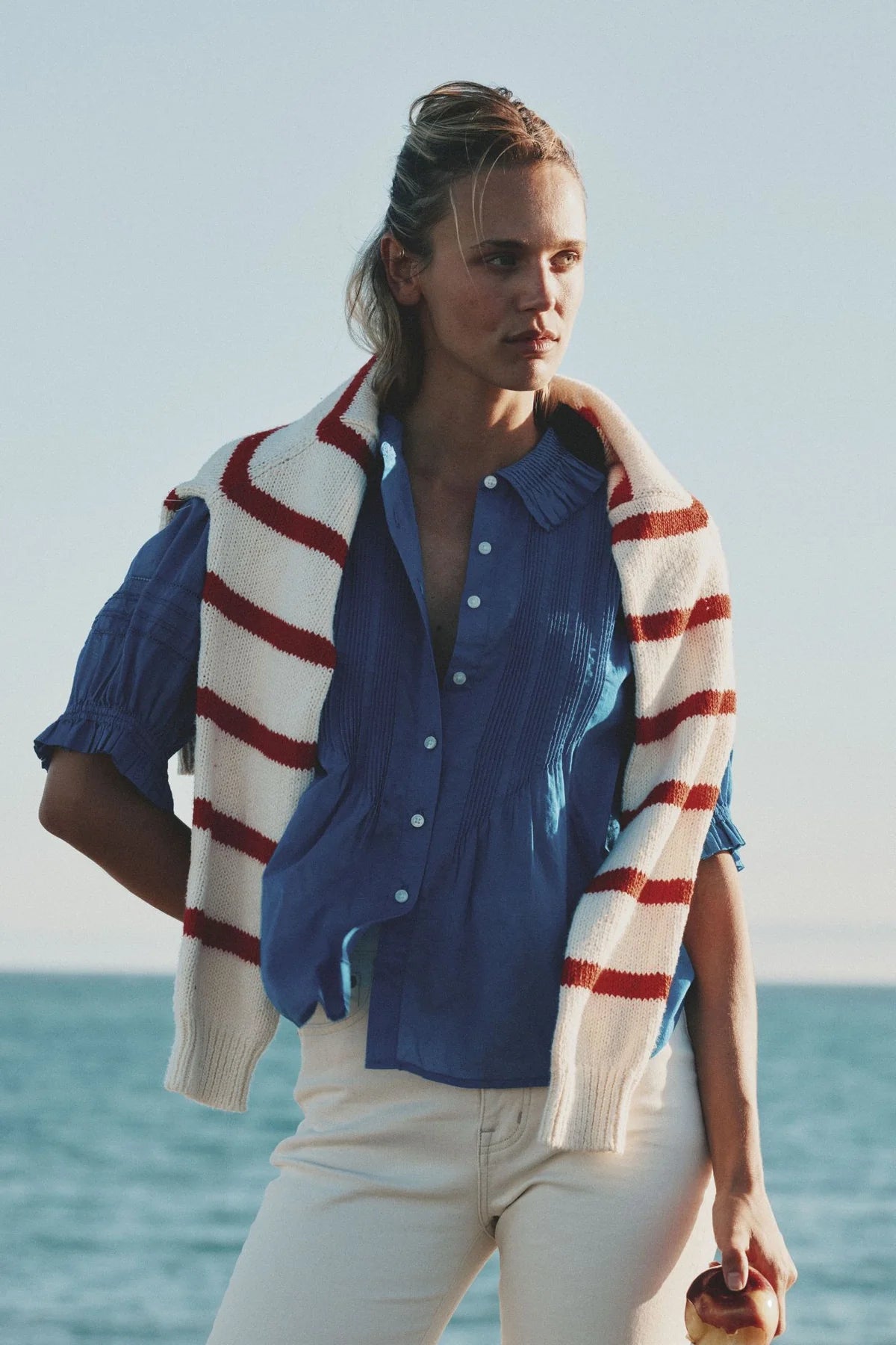 Woman wearing Trovata Jess blue button-up blouse with red and white striped cardigan by the ocean