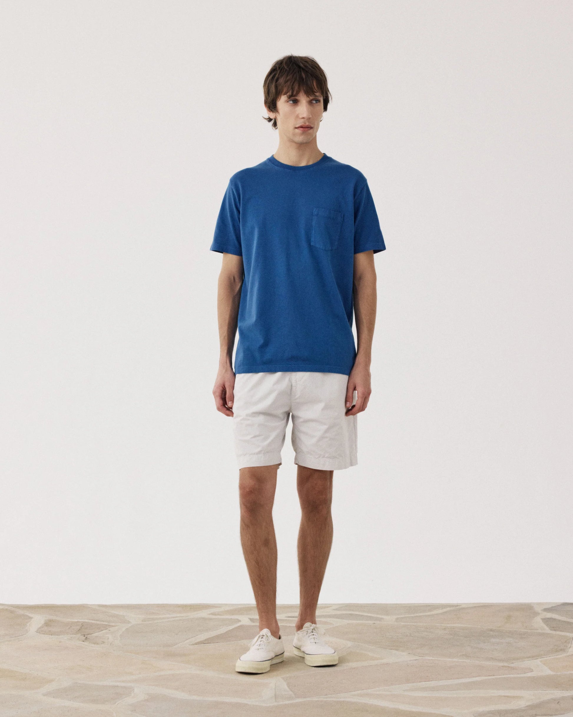 Man wearing Hartford blue crew neck t-shirt with white Joggy Short Flax casual shorts and white sneakers.