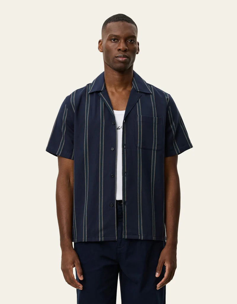 Les Deux Lawson short-sleeve striped shirt in dark navy with vertical stripes, worn open over white tee.
