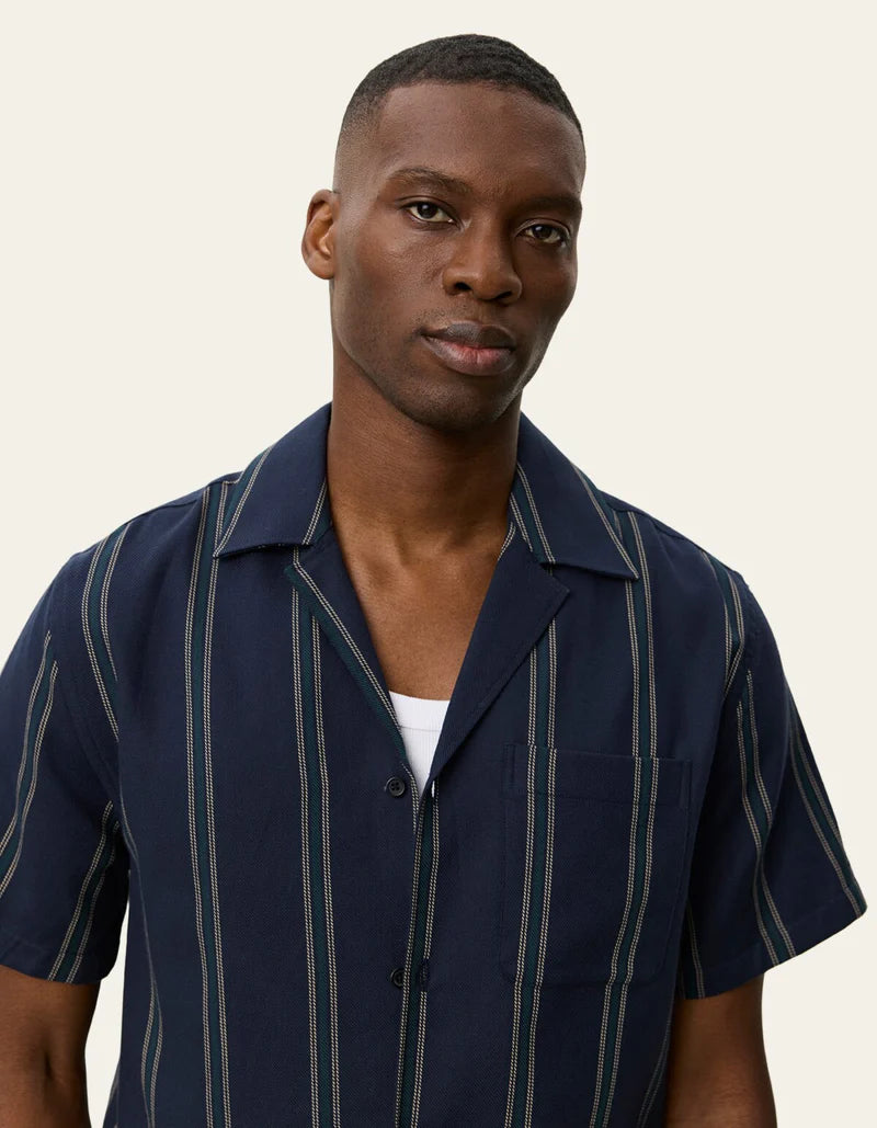 Les Deux Lawson short-sleeve striped shirt in dark navy with vertical pinstripes, worn open over white tee.