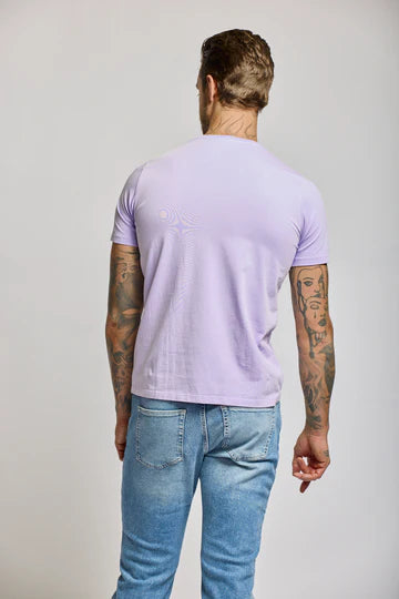 Back view of man wearing Easy Mondays lilac crew neck t-shirt with blue jeans, showing tattoos on both arms.