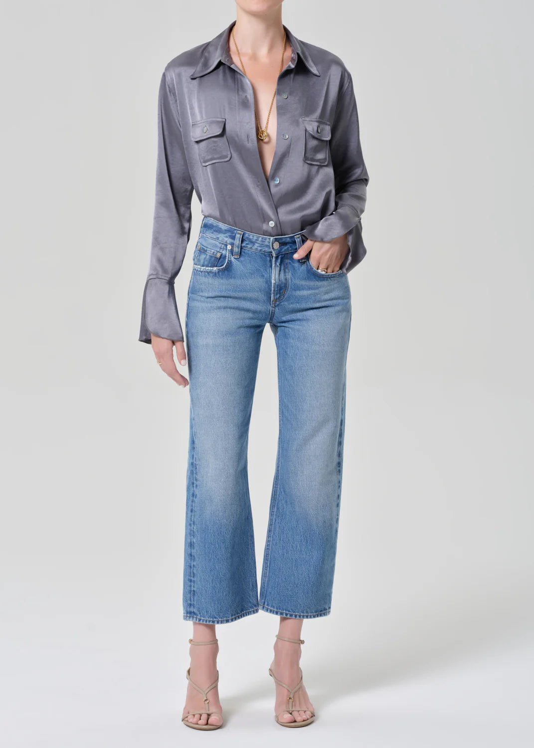 Woman wearing Citizens of Humanity Faye Vintage Straight jeans in light blue denim with grey button-up shirt and strappy h...