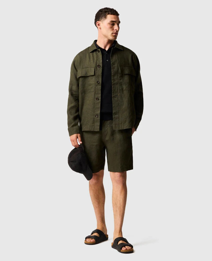 Man wearing Rodd & Gunn olive green linen shirt and matching shorts with black polo and sandals.