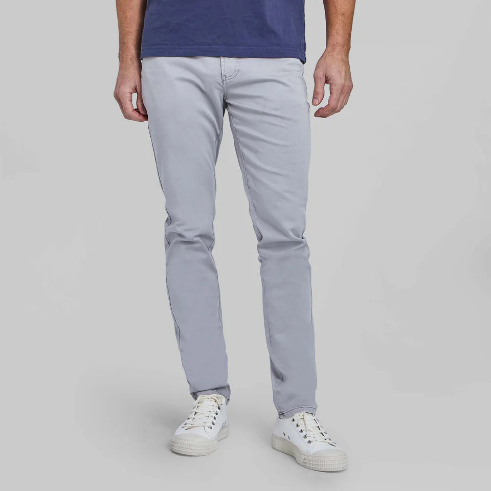 Man wearing light gray stretch comfort chinos with white sneakers and navy shirt, showing relaxed fit styling.