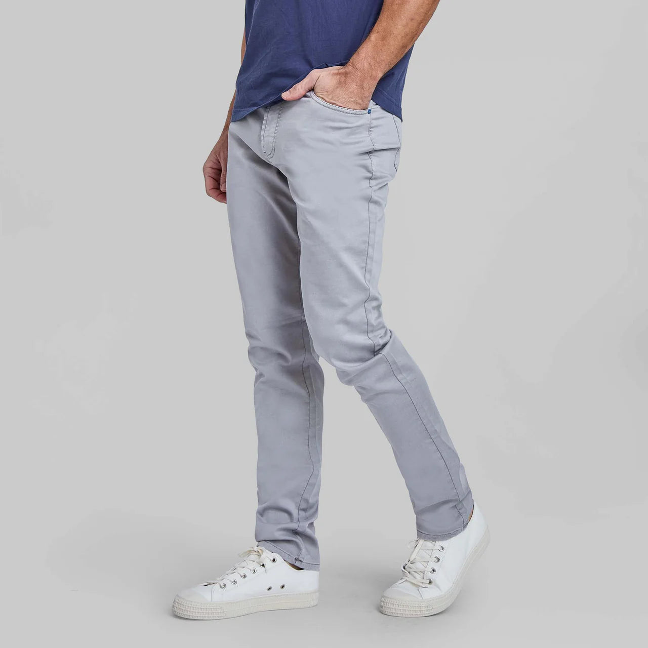 Man wearing Rye 51 Flex light gray stretch pants with five pockets, navy shirt, and white sneakers.