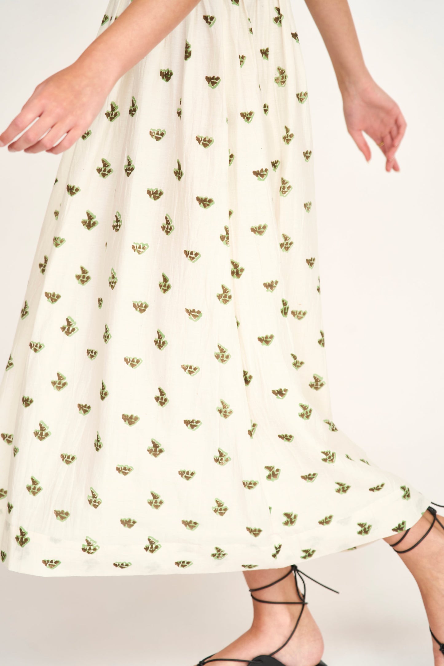Model wearing cream midi dress with small green and brown botanical print pattern and lace-up shoes