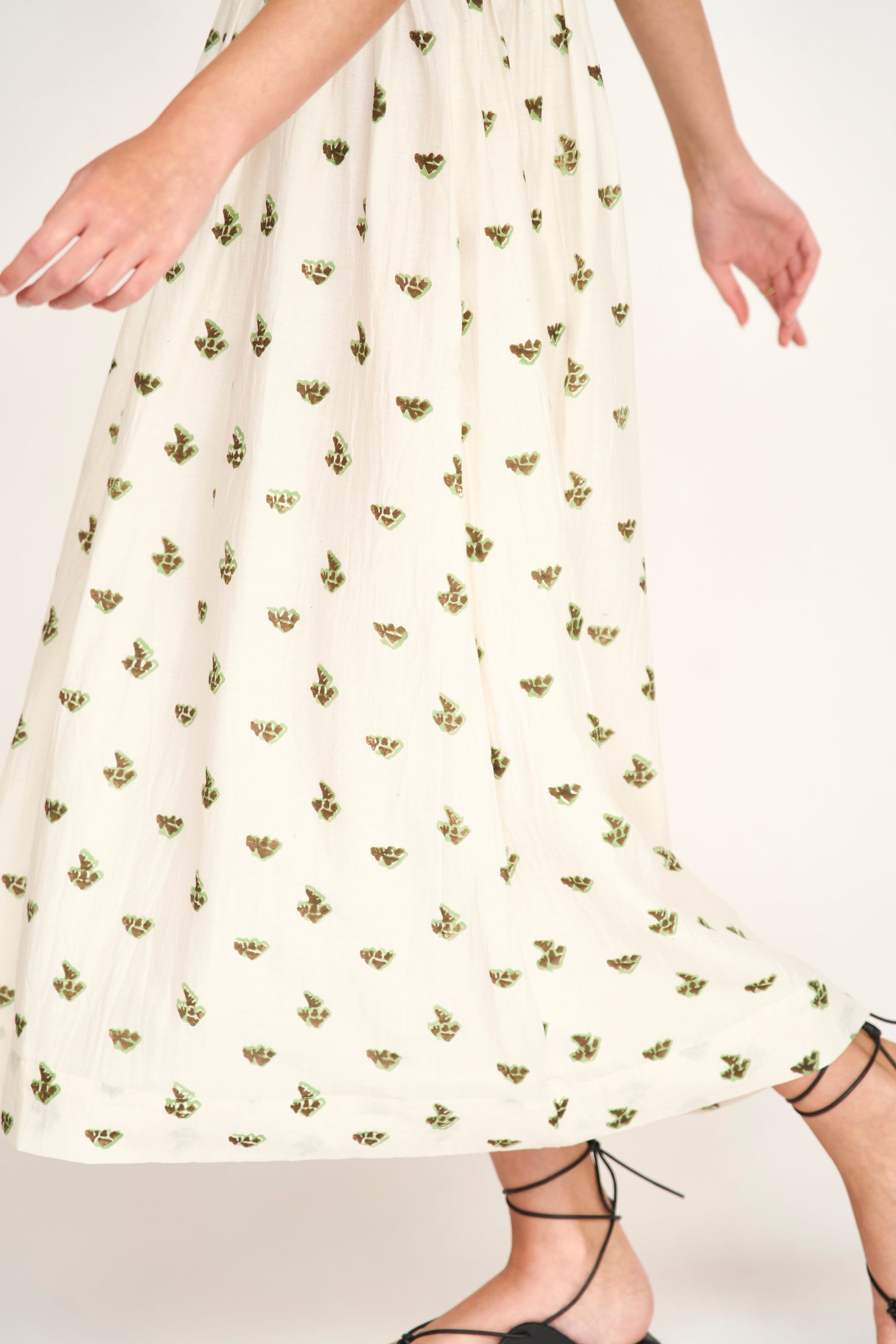 Model wearing cream midi dress with small green and brown botanical print pattern and lace-up shoes