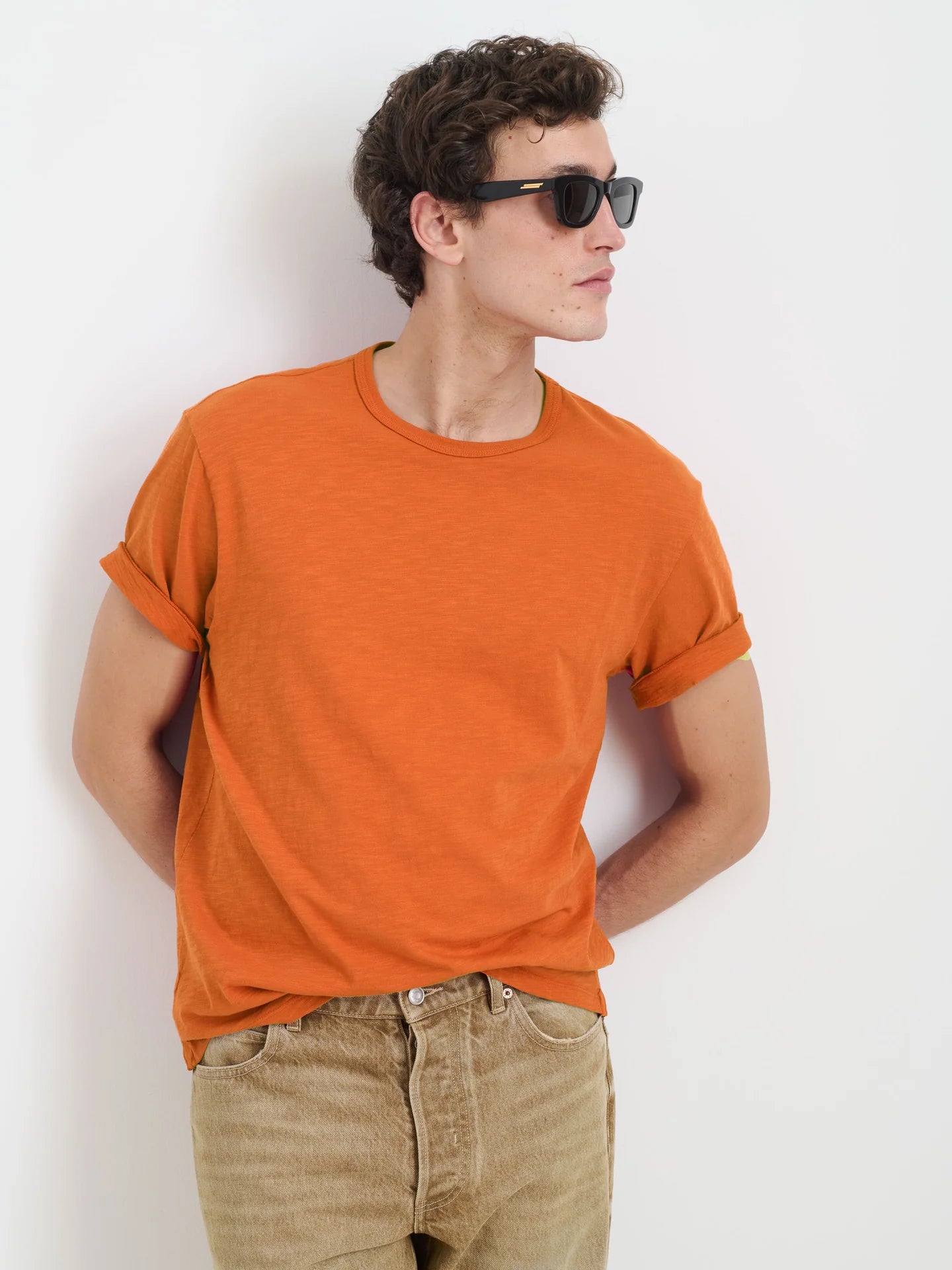 Alex Mill Standard orange slub cotton t-shirt on male model wearing sunglasses and beige jeans against white background.