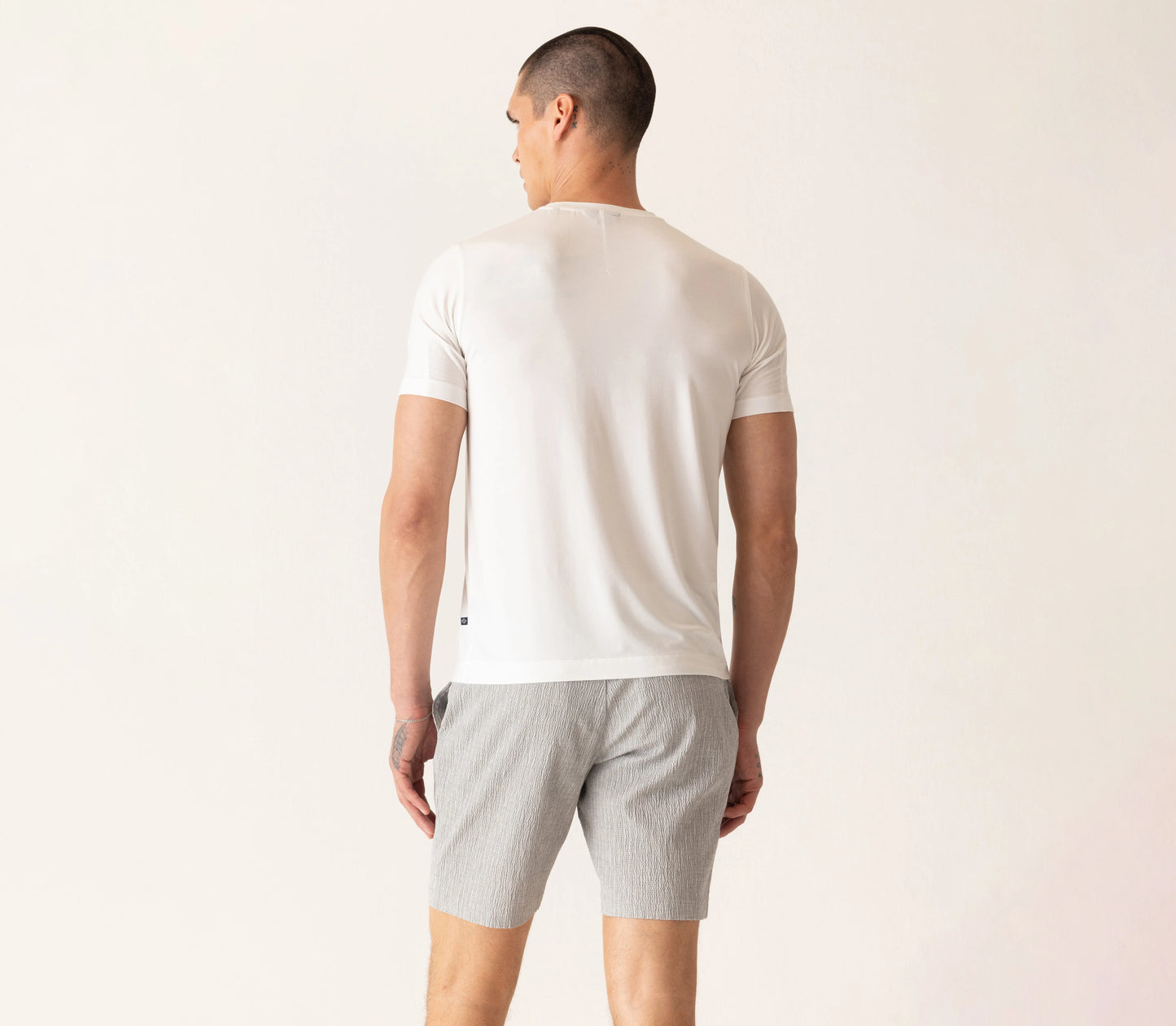 Man wearing white Deke SS Modern crew neck t-shirt and gray shorts, shown from behind in casual styling.