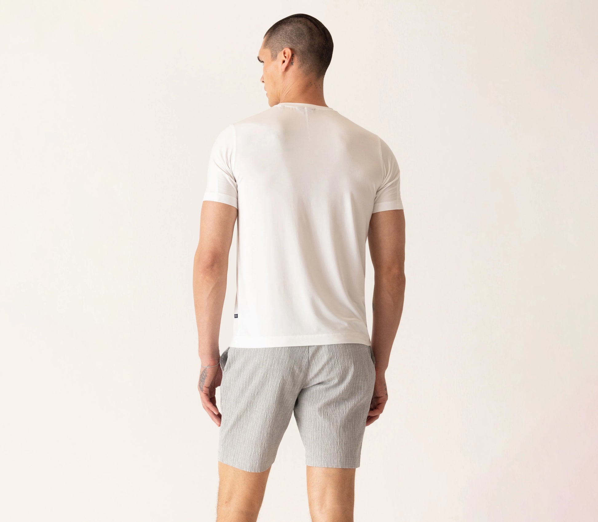 Man wearing white Deke SS Modern crew neck t-shirt and gray shorts, shown from behind in casual styling.