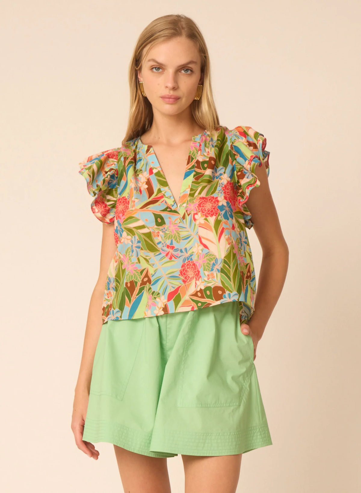 Gilner Farrar Orla Blouse in tropical Amazonian print with ruffled sleeves and V-neck, styled with green shorts.