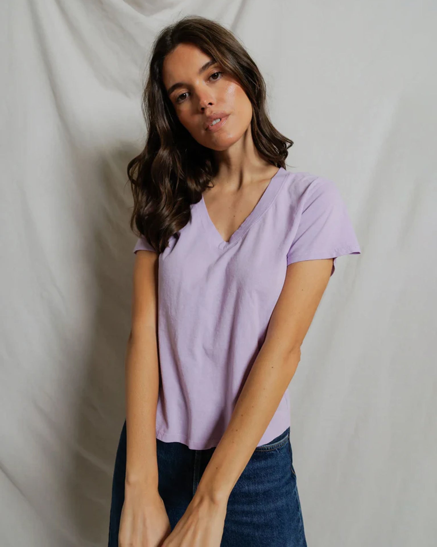 Woman wearing light purple v-neck short sleeve tee with jeans against white backdrop