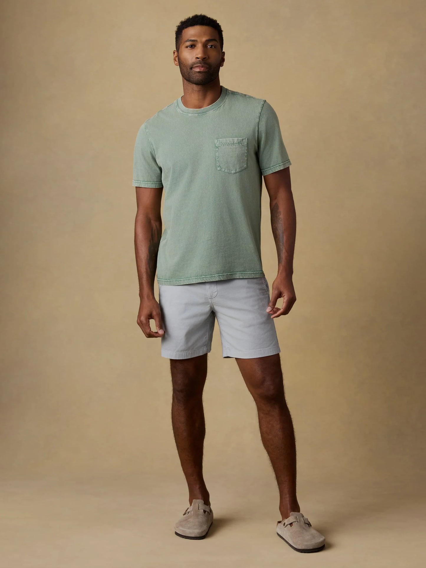 Man wearing Faherty Essential Chino Shorts in light grey with green pocket t-shirt and suede loafers