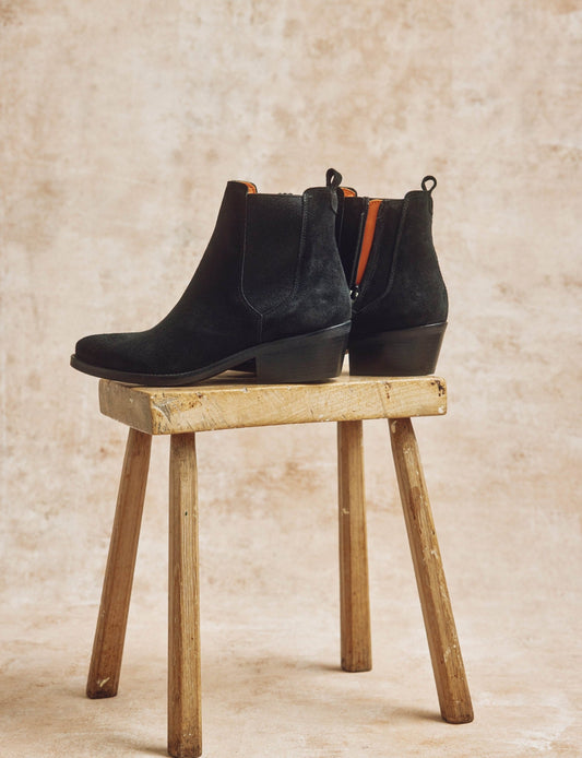 Pair of black suede ankle boots with block heel displayed on rustic wooden stool