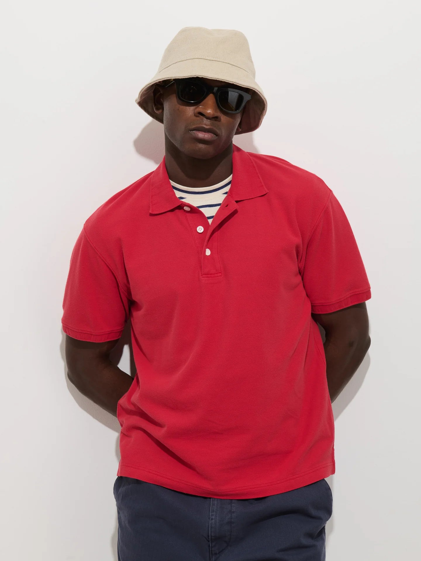 Man wearing Alex Mill Ryan short sleeve pique polo shirt in red with beige bucket hat and sunglasses