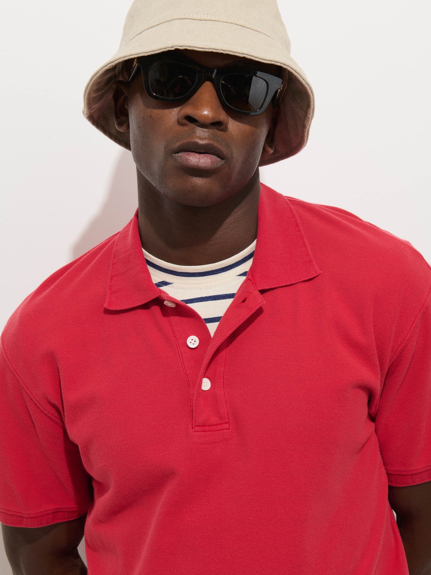 Alex Mill Ryan short sleeve pique polo shirt in vintage red with collar and button placket worn by model with striped shir...