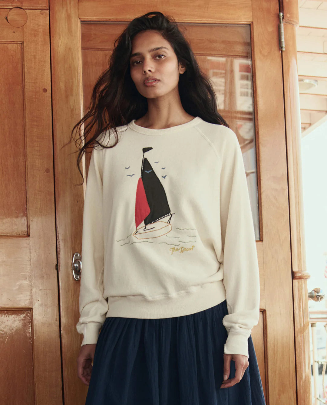 The GREAT College Sweatshirt featuring sailing boat applique design in washed white, worn with navy skirt.