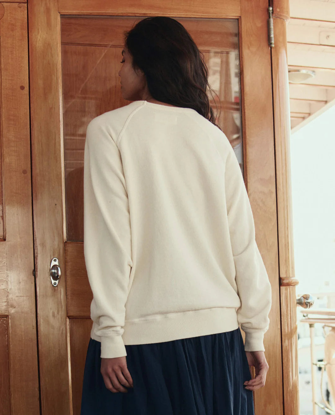 Back view of woman wearing The GREAT College Sweatshirt with sailing boat applique in cream white.