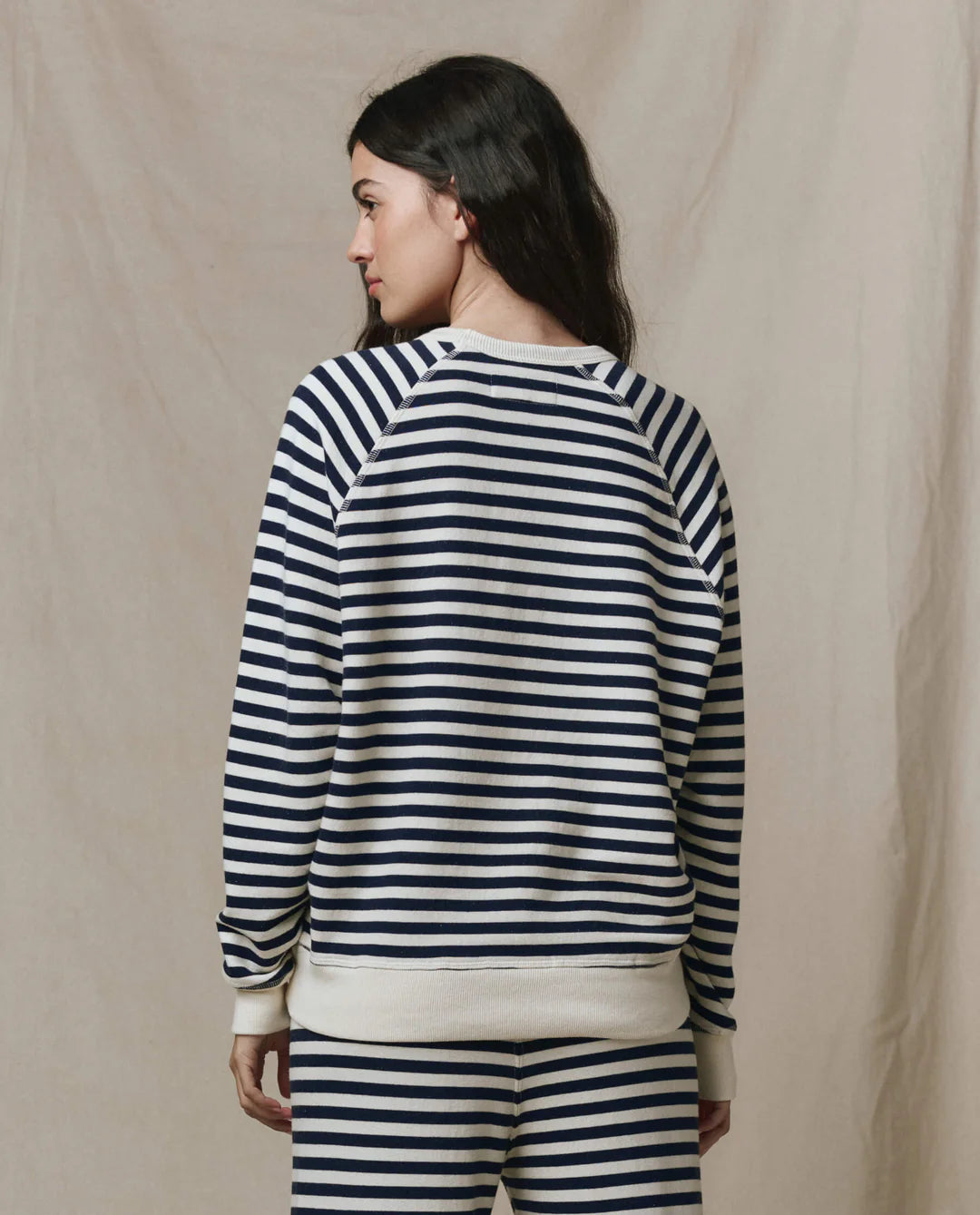 Woman wearing The GREAT College Sweatshirt in navy and white sailor stripes, shown from behind in relaxed fit.
