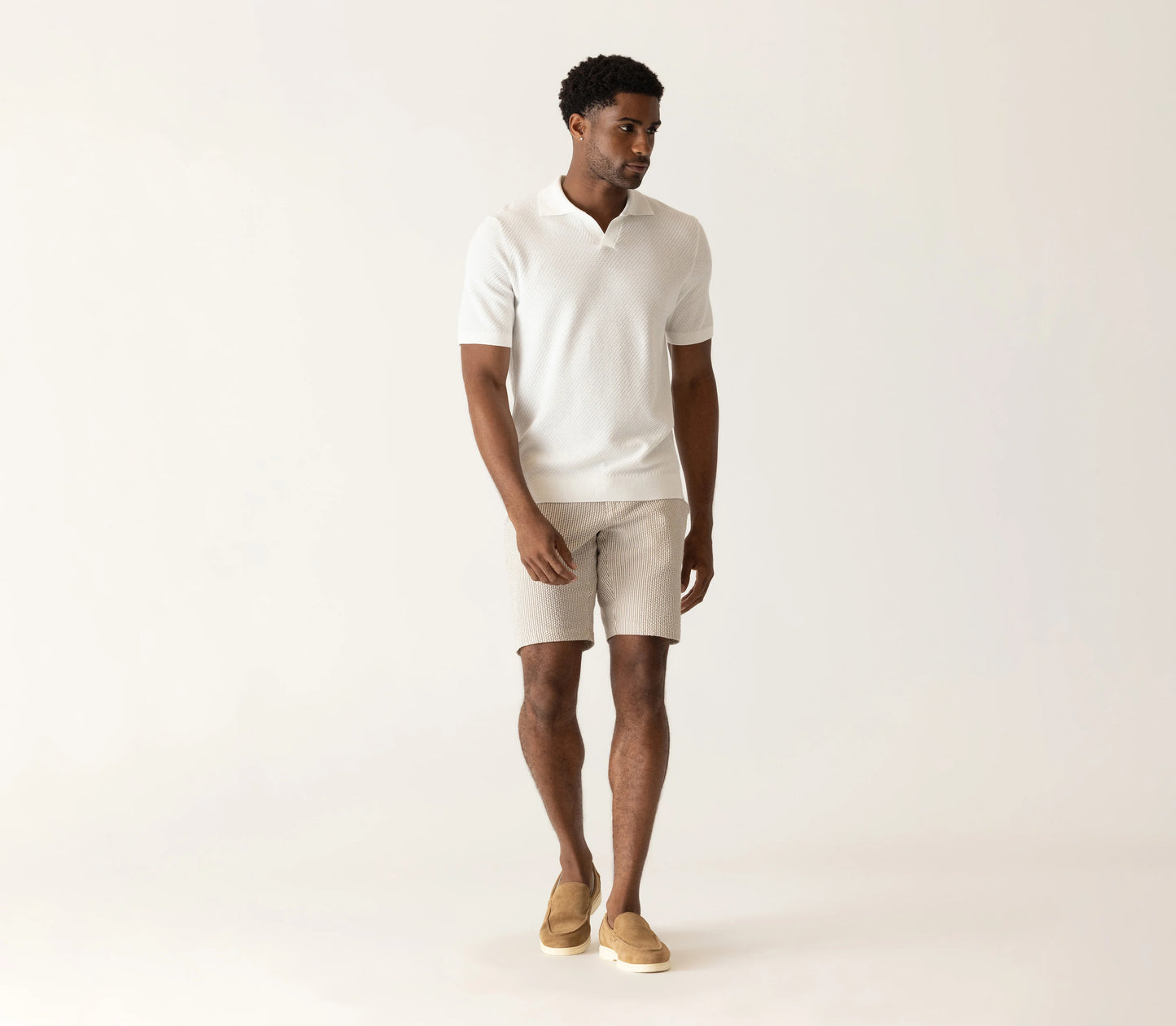 Man wearing white textured polo shirt and beige striped seersucker bermuda shorts with tan slip-on shoes.
