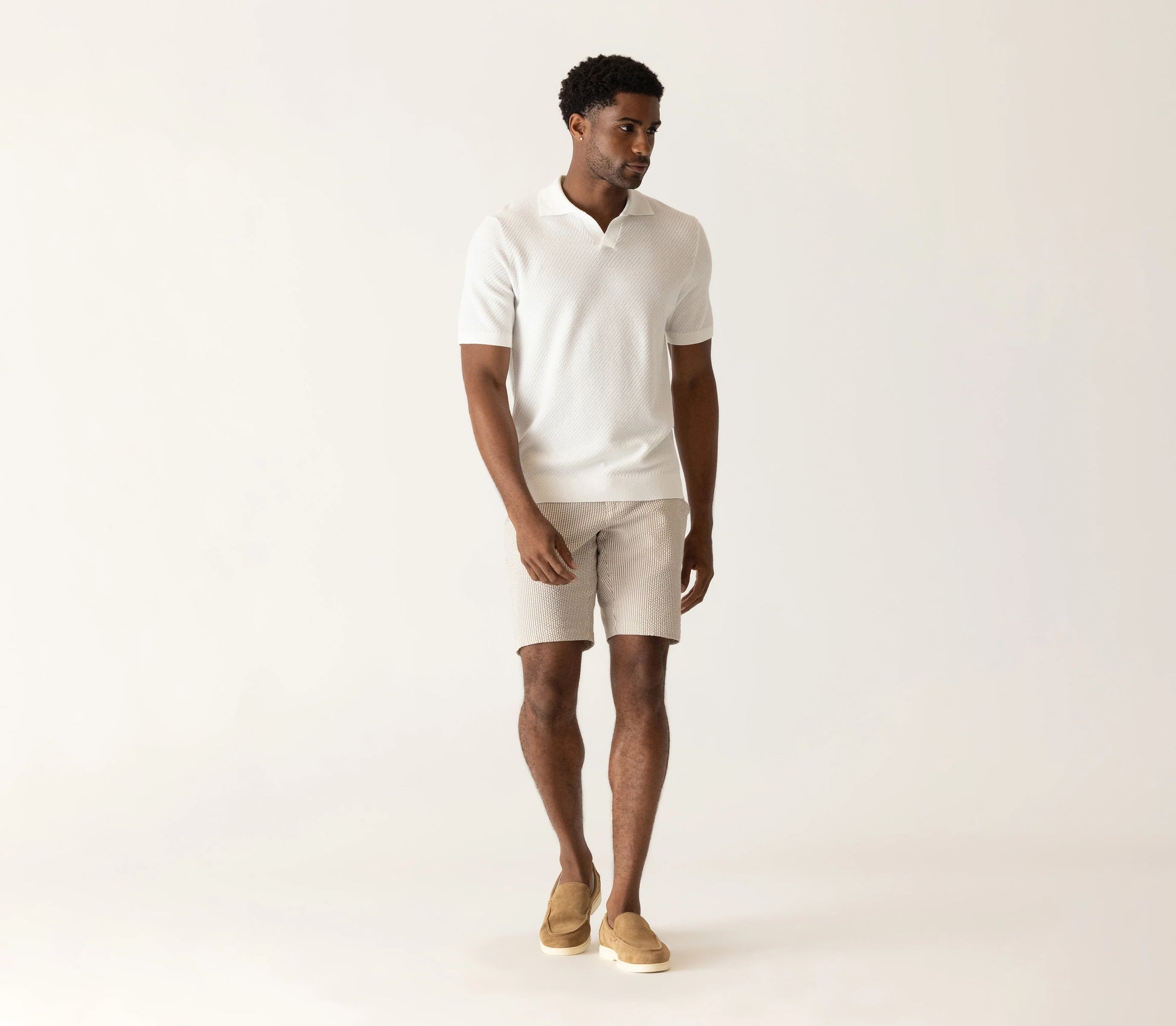 Man wearing white textured polo shirt and beige striped seersucker bermuda shorts with tan slip-on shoes.
