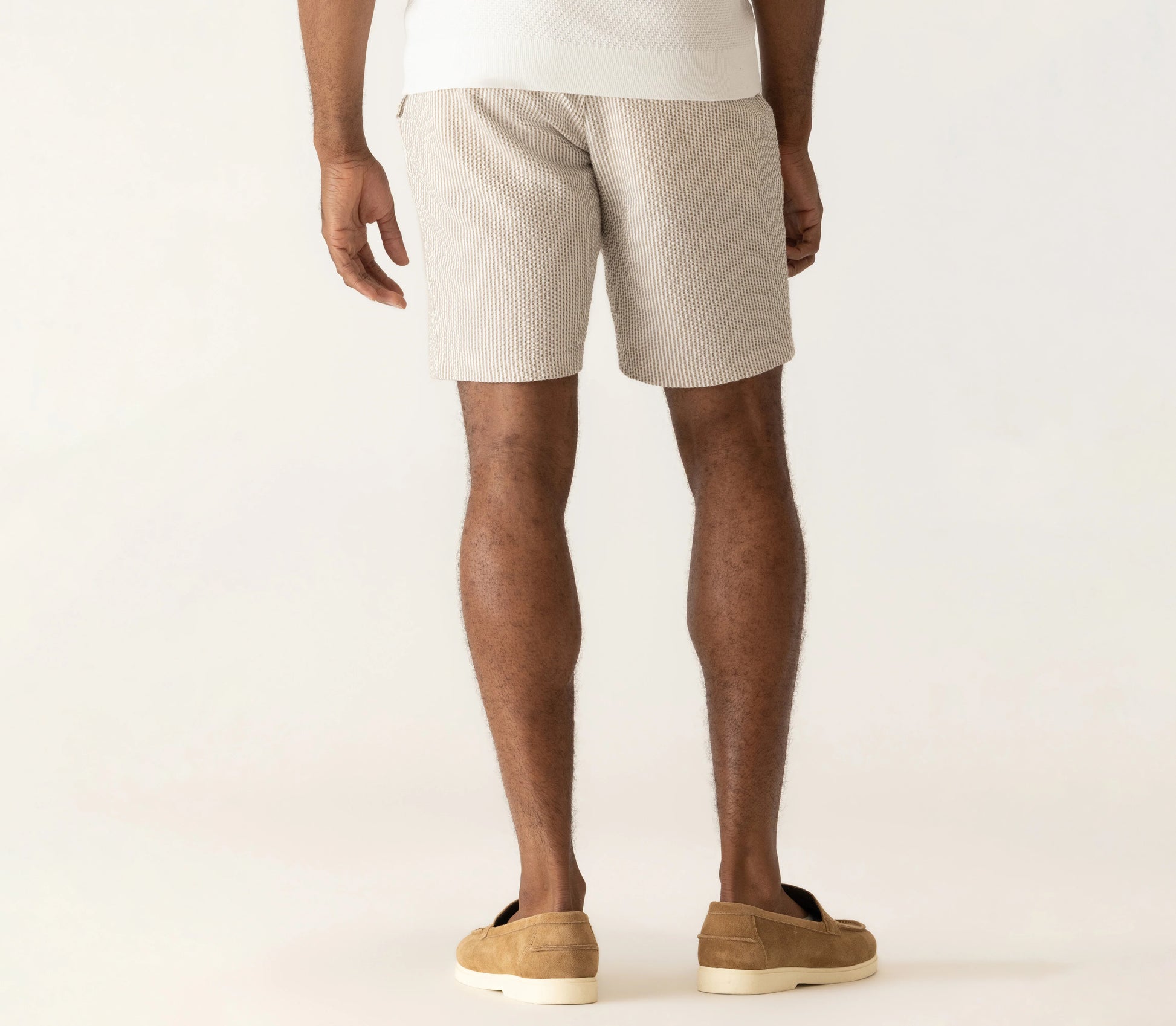 Man wearing Deke Oasis Bermuda shorts in textured seersucker fabric with brown suede loafers on neutral background.