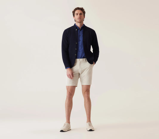 Man wearing beige Bermuda shorts styled with navy cardigan and blue shirt in casual smart outfit.