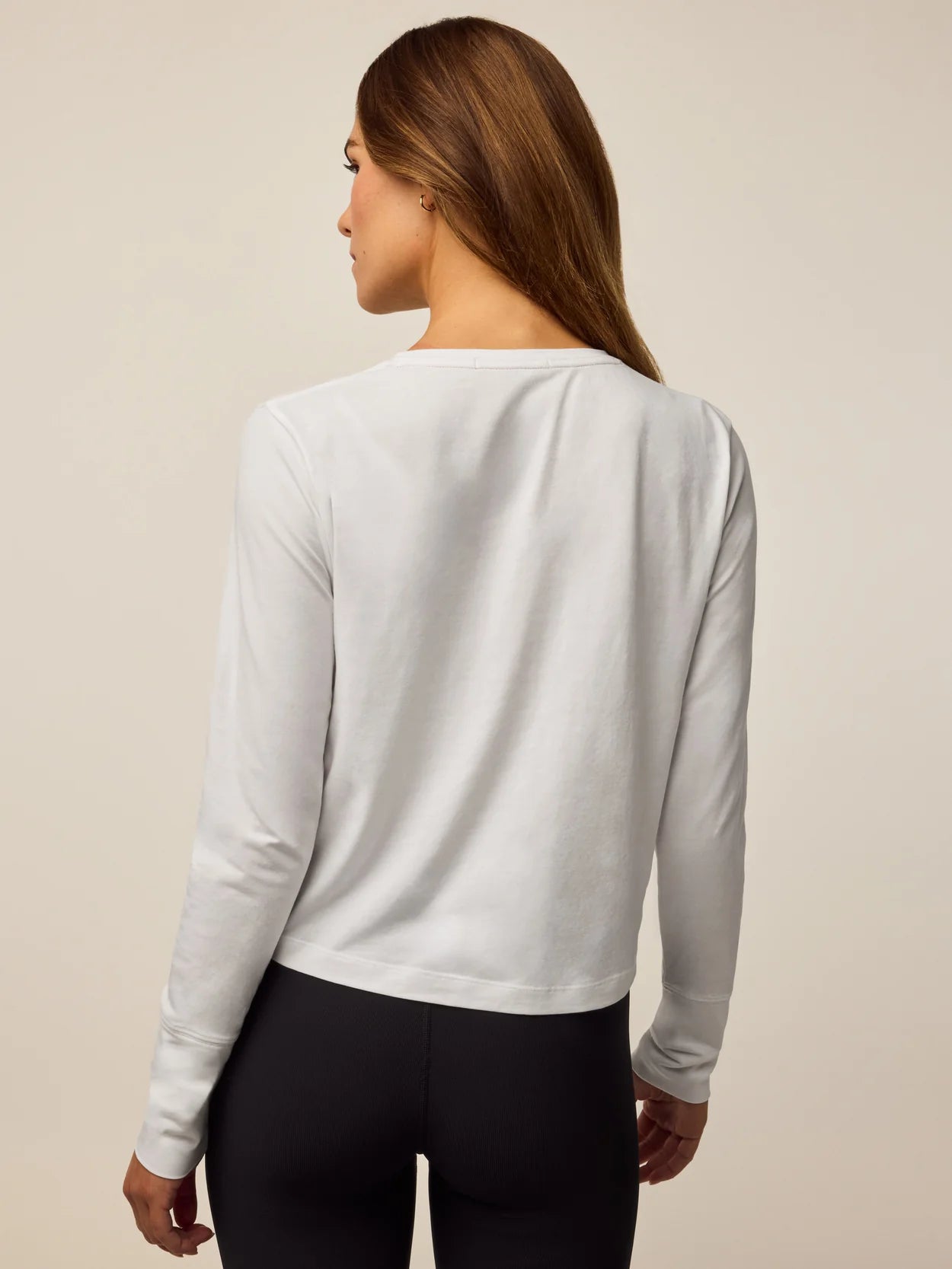 Woman wearing Greyson long sleeve Sloane top in arctic white, shown from behind with black leggings.