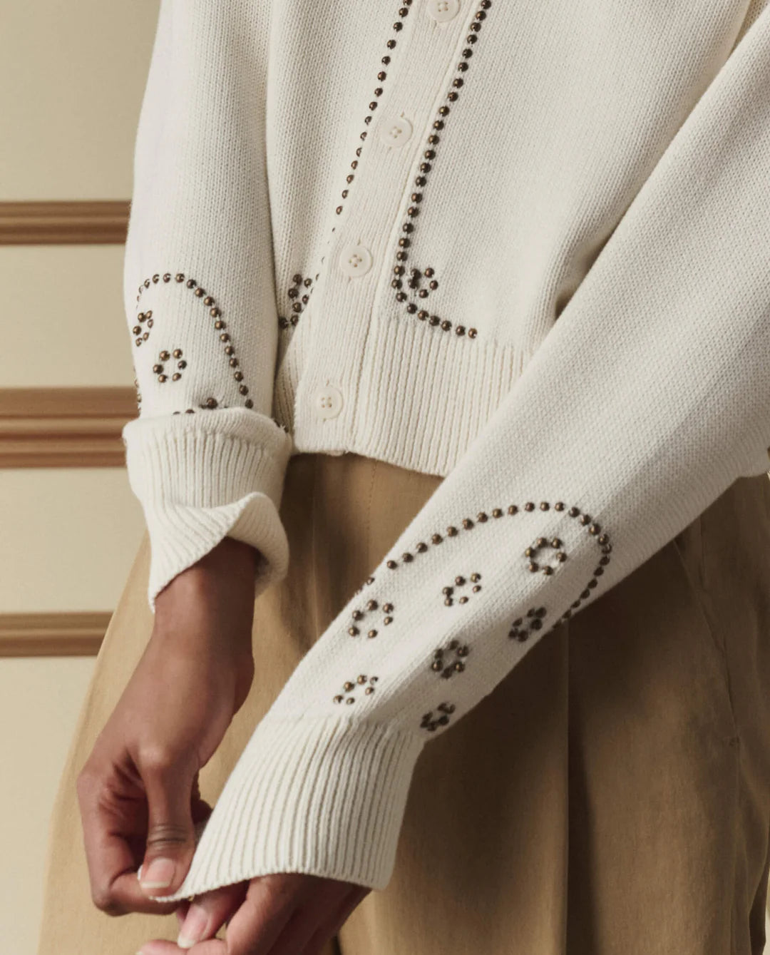 The Great cream studded cardigan with metal stud embellishments on sleeves and button placket, ribbed cuffs visible.