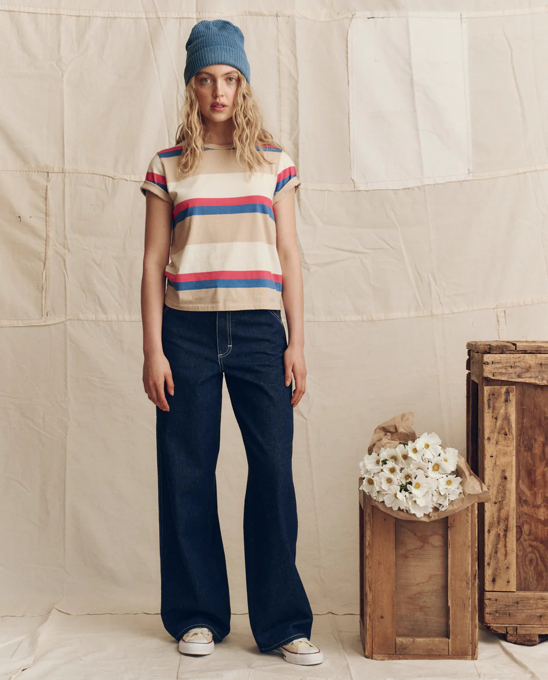 Woman wearing The Great striped short-sleeve tee with wide-leg jeans and blue beanie in casual outfit styling.