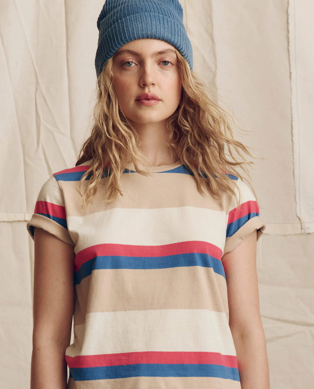 Woman wearing The Great striped short-sleeve tee with blue beanie against neutral background