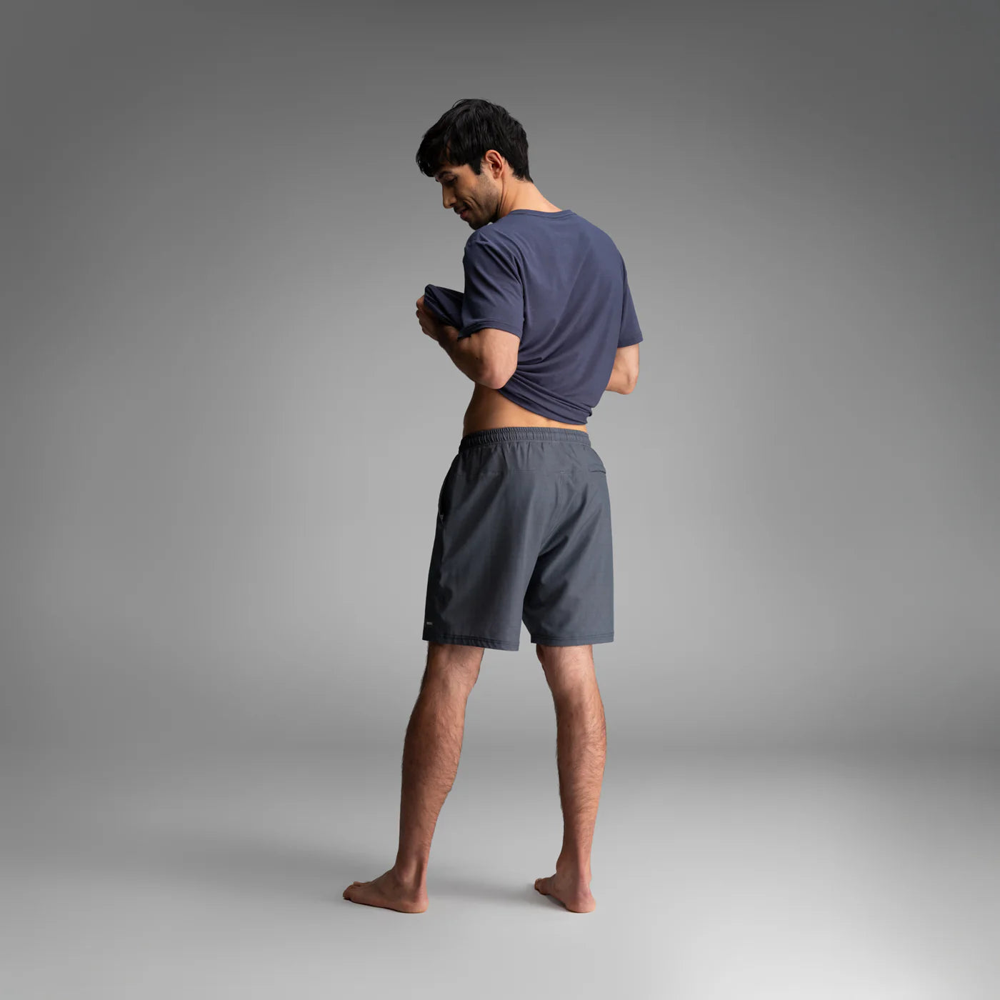 Man wearing BN3TH Shoreline 2-in-1 athletic shorts and t-shirt, standing barefoot against gray background