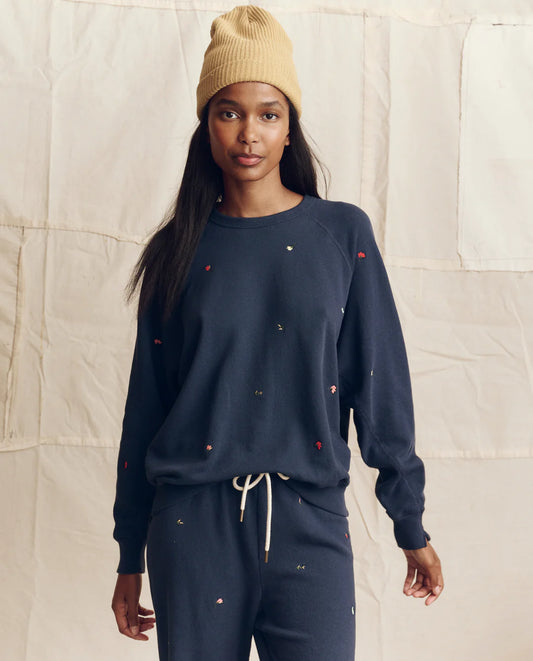Woman wearing The Great navy blue college sweatshirt with colorful floral embroidery and matching sweatpants, styled with ...