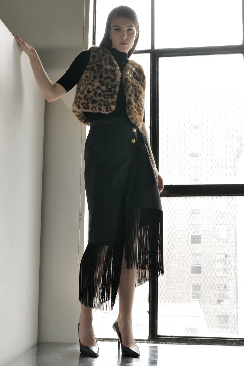 Woman wearing Le Superbe Superfluff leopard print faux fur vest over black turtleneck and fringed skirt