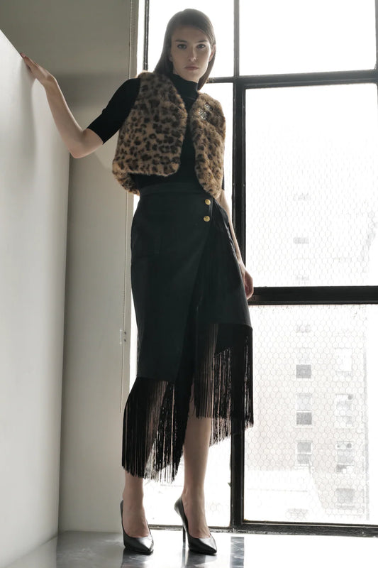 Woman wearing Le Superbe Superfluff leopard print faux fur vest over black turtleneck and fringed skirt
