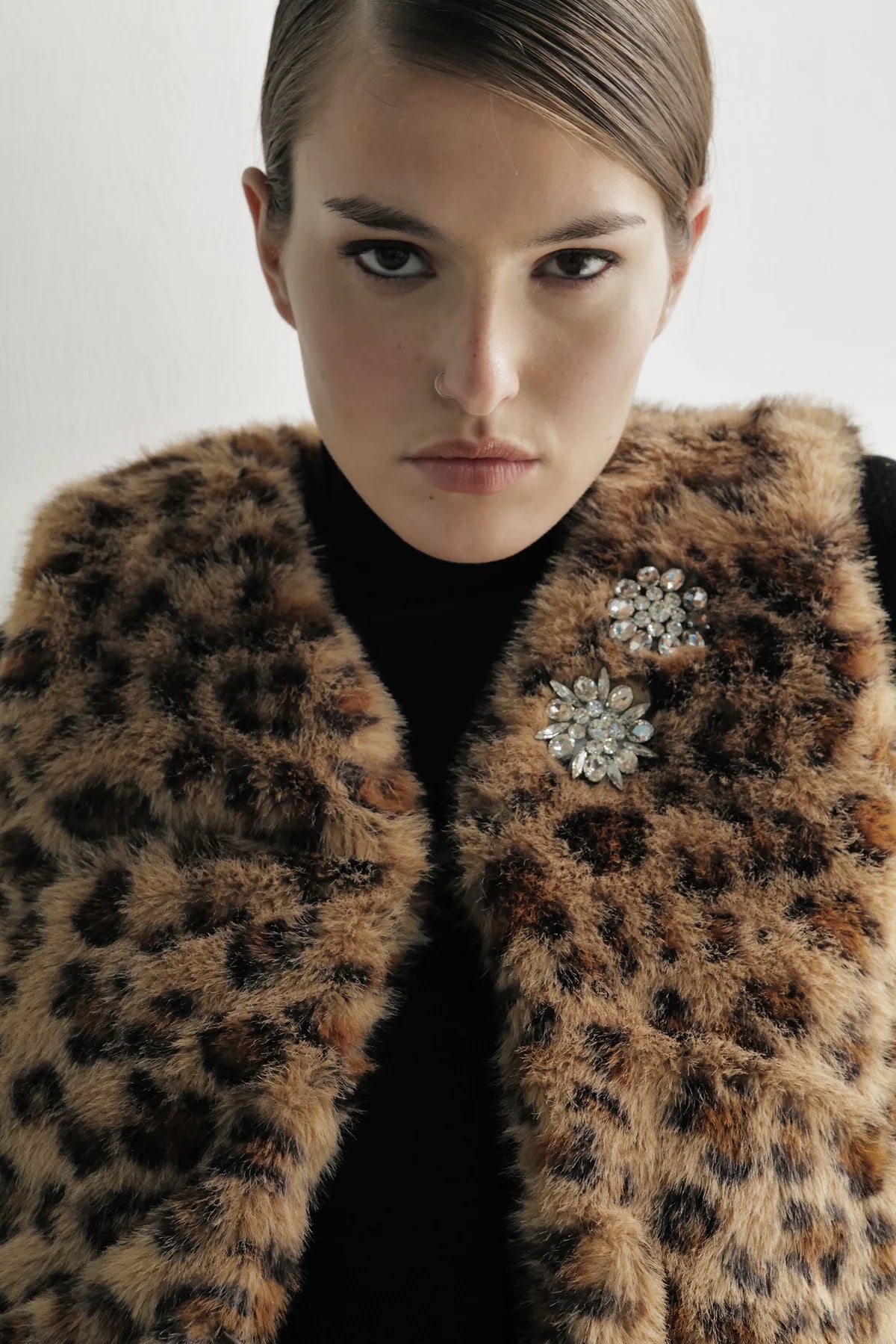Woman wearing Le Superbe leopard print faux fur vest with crystal brooch detailing over black top.