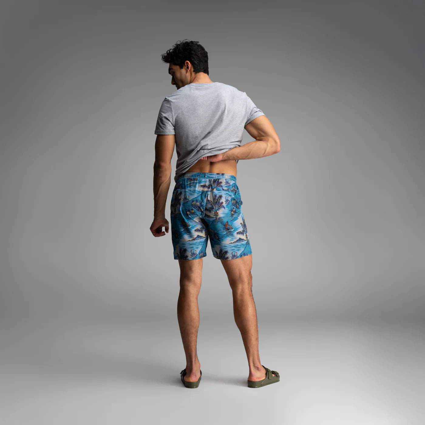 Man wearing BN3TH tropical print swim shorts and gray t-shirt, shown from behind in studio setting.