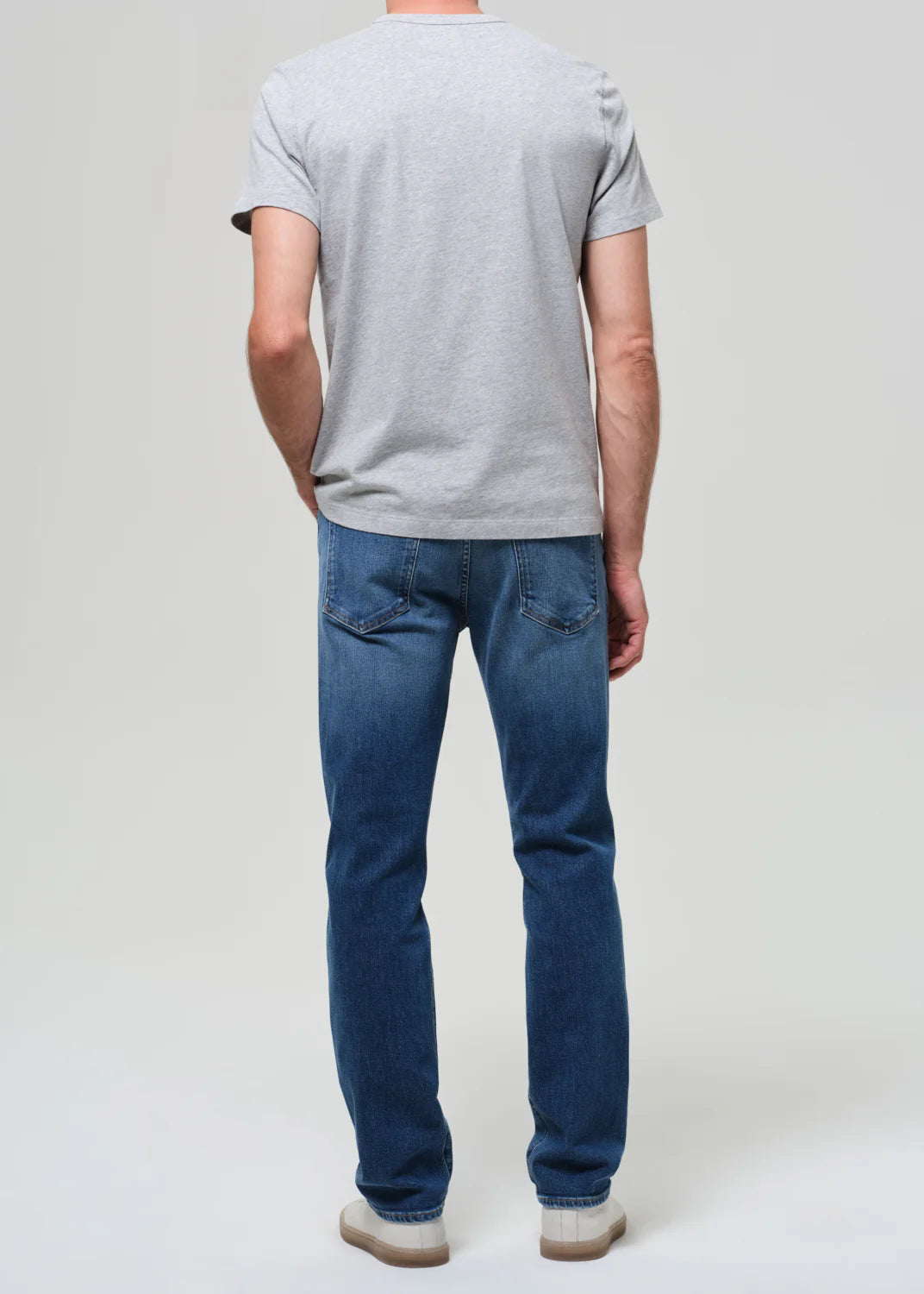 Man wearing Citizens of Humanity Elijah jeans in true blue denim with grey t-shirt, shown from behind.