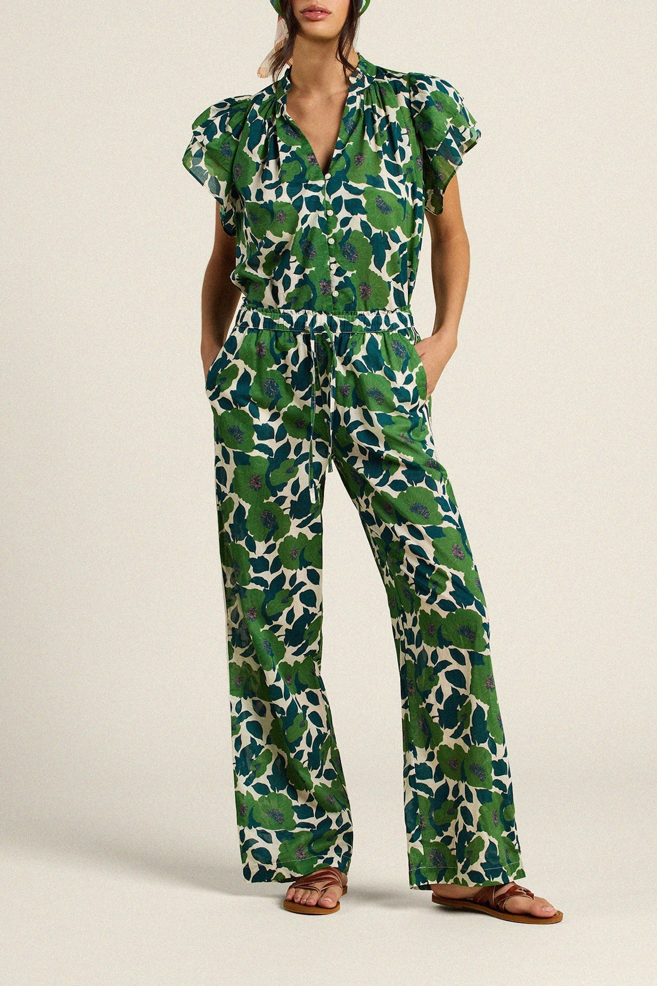 Woman wearing green floral print jumpsuit with flutter sleeves and wide leg pants
