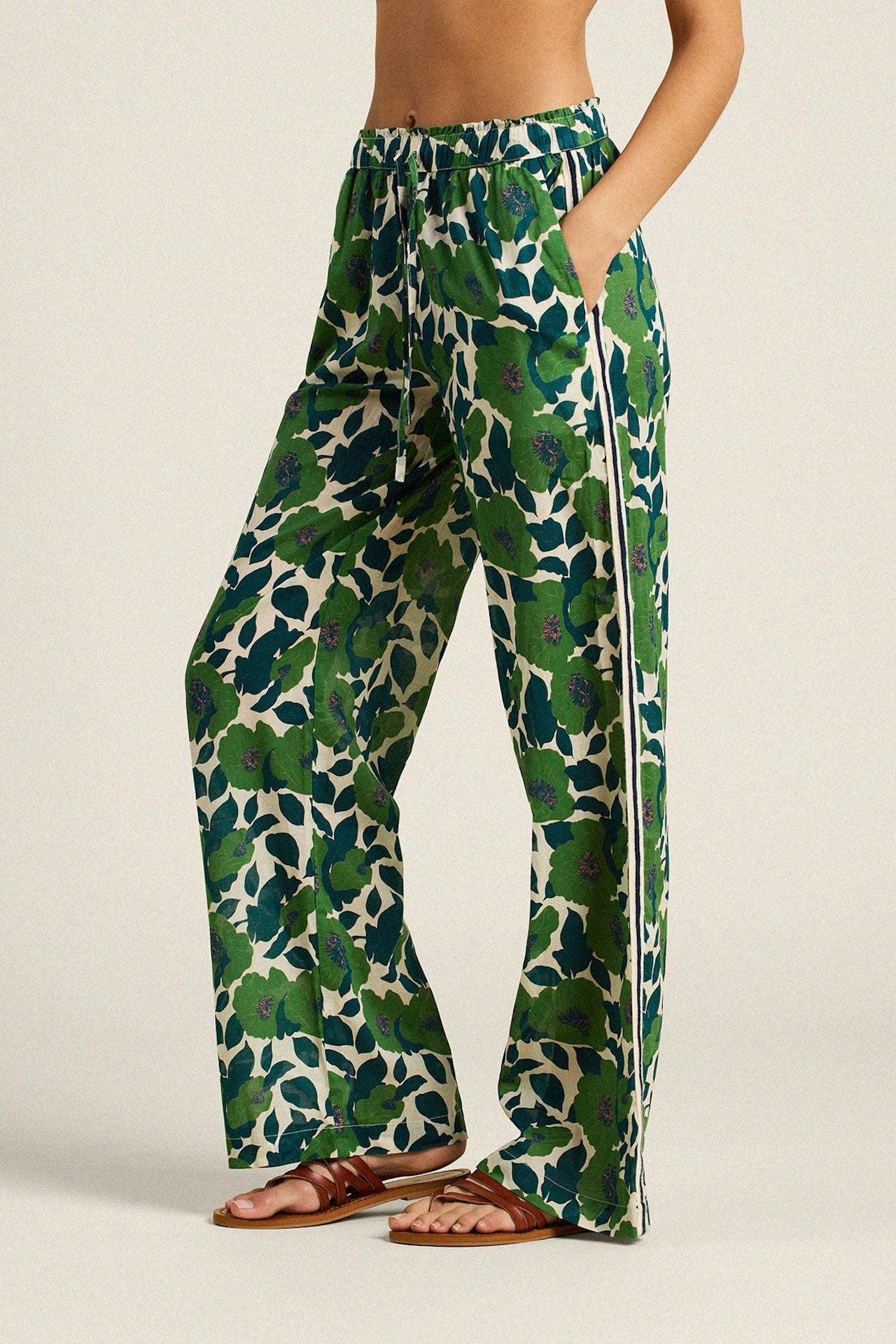 Woman wearing wide-leg floral print pants with green leaves and flowers on cream background