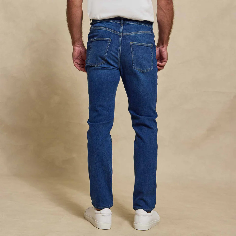 Man wearing Rye 51 Stretch blue denim jeans and white sneakers, shown from behind against beige background.