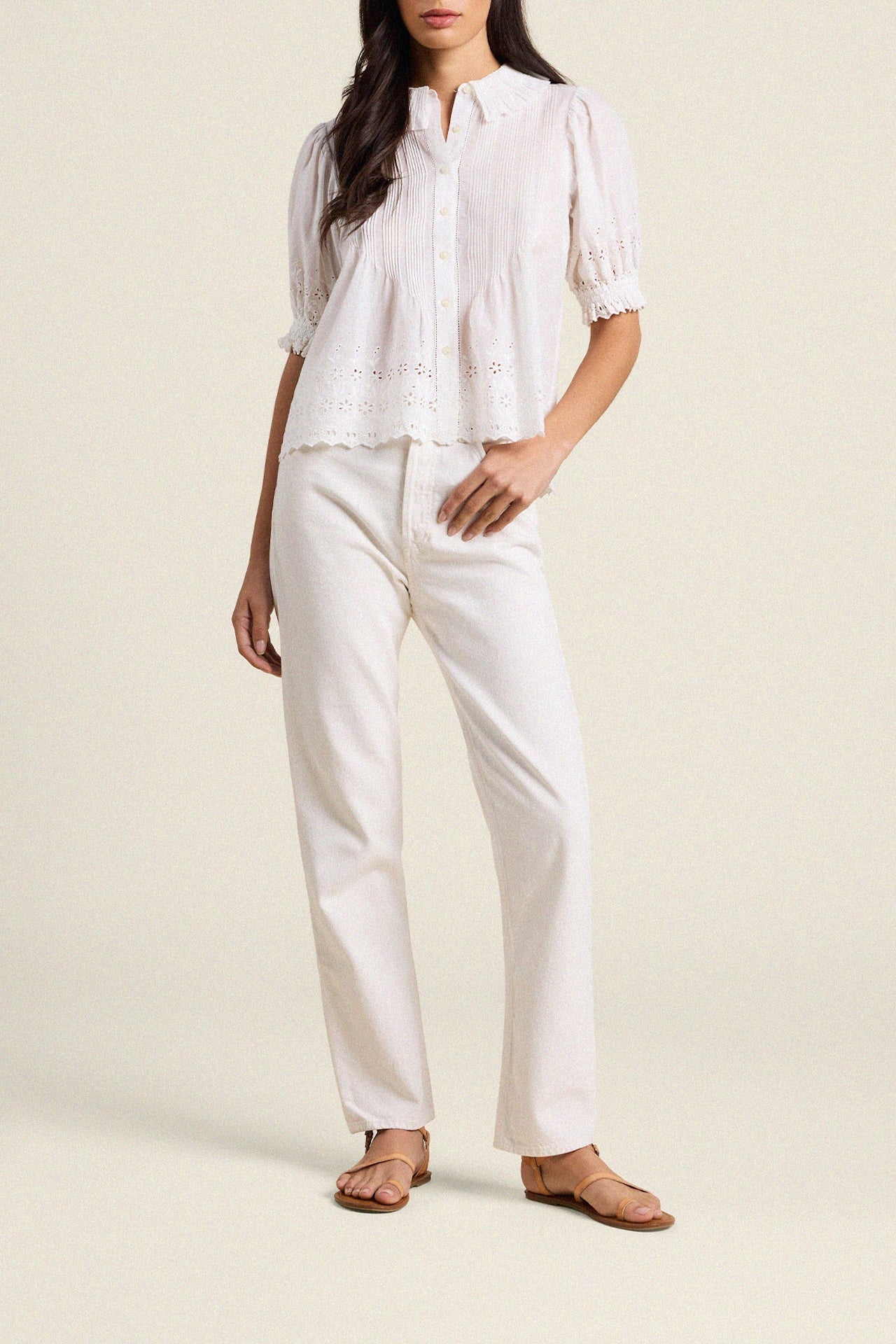 Woman wearing white eyelet blouse with puffed sleeves and white pants in professional studio setting