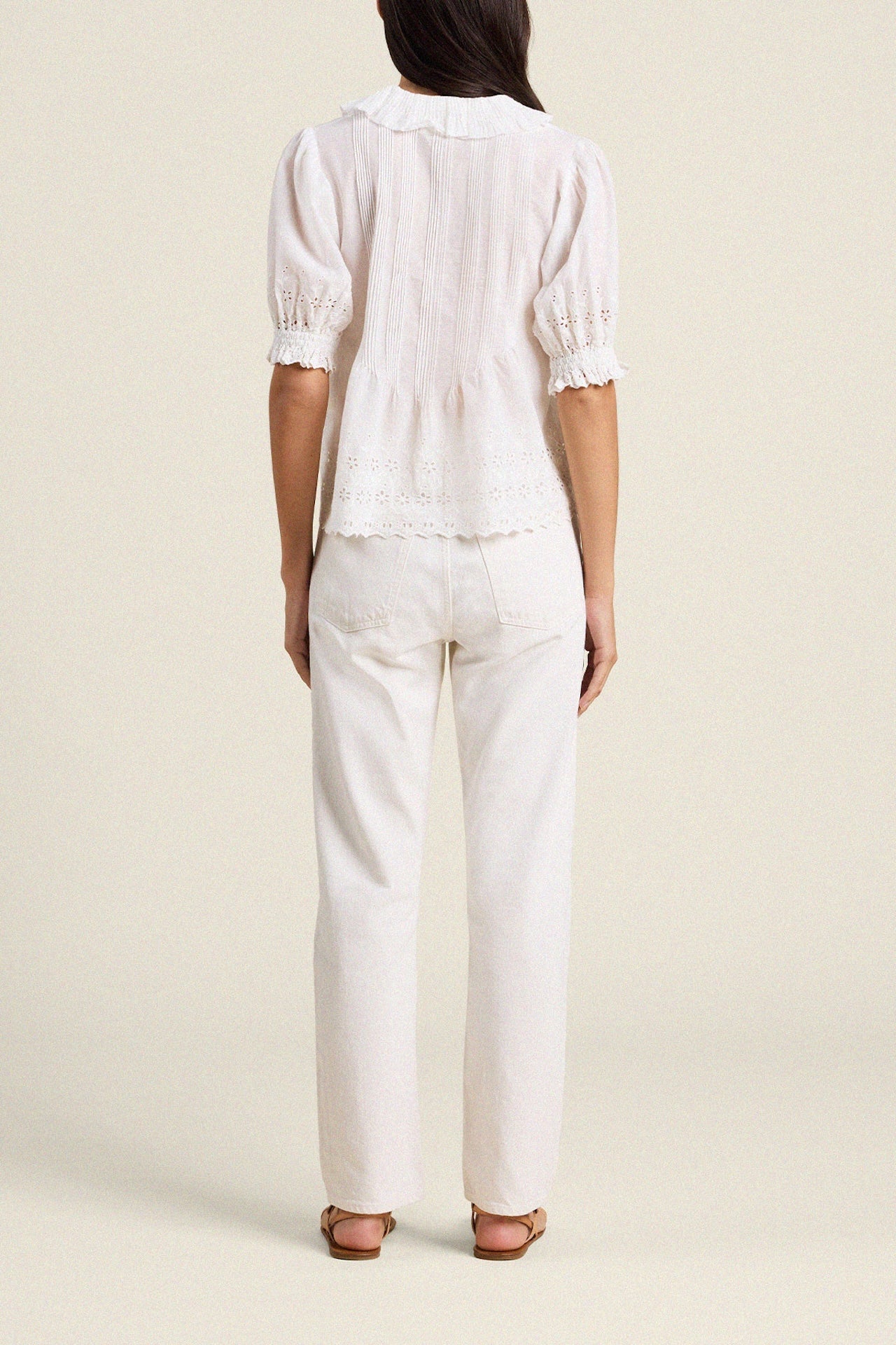 Back view of woman wearing white eyelet blouse with puffed sleeves and white pants